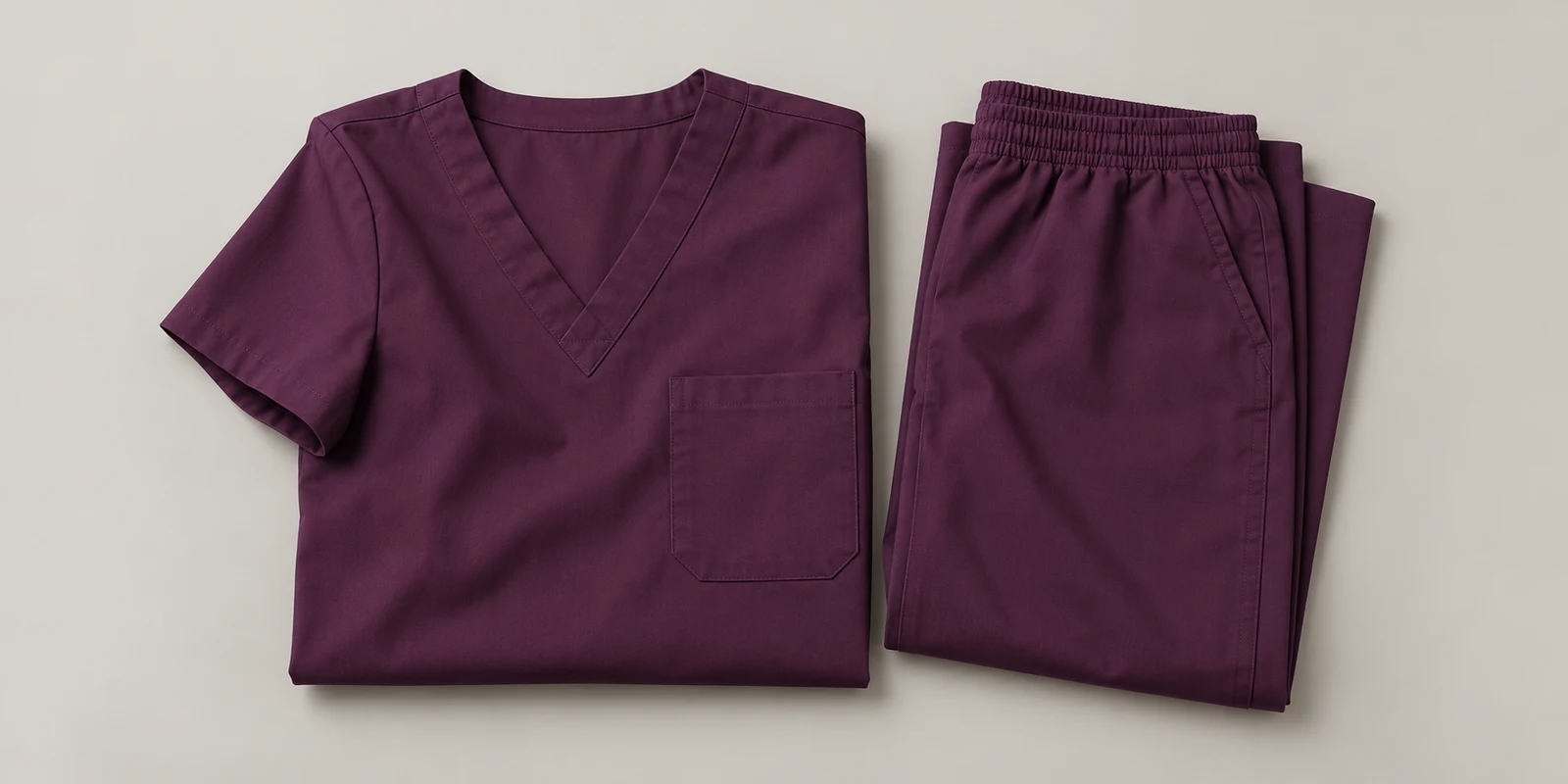 Illustrative plum folded medical scrub set showing fabric and waistband details on warm-grey background