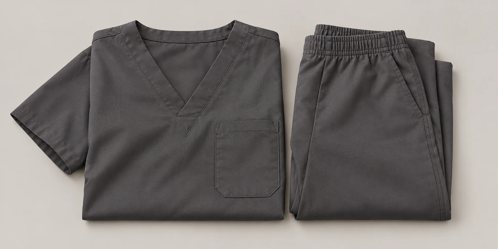Illustrative warm charcoal folded medical scrub set showing fabric and waistband details on warm-grey background