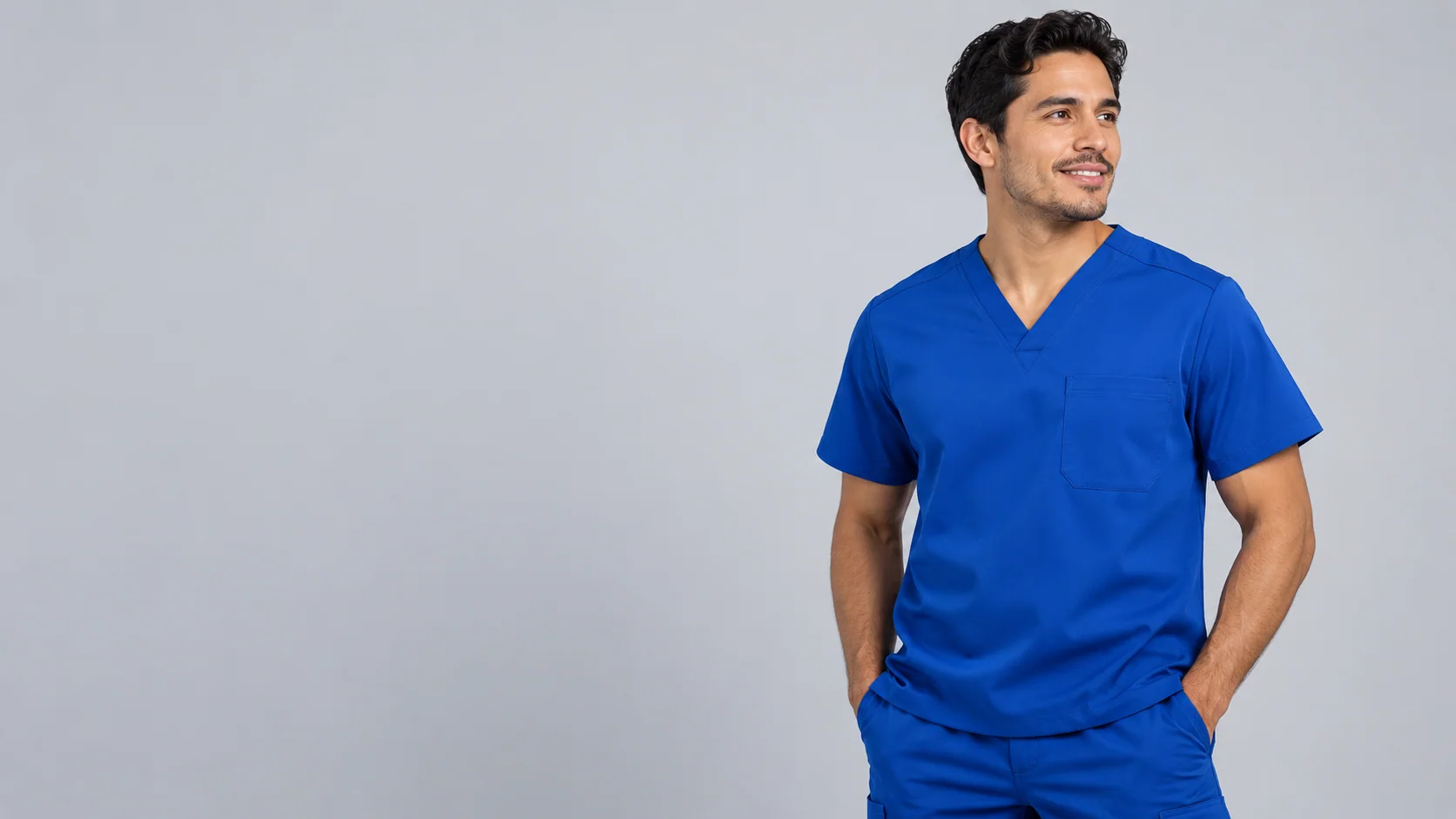 Man wearing a pale grey scrub top and cuffed jogger trousers against a plain background
