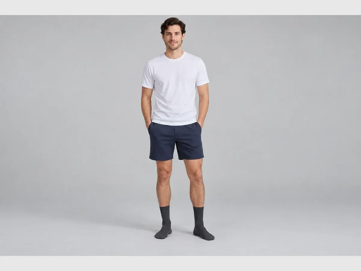 Person wearing dark socks with a white shirt and navy shorts against a grey background